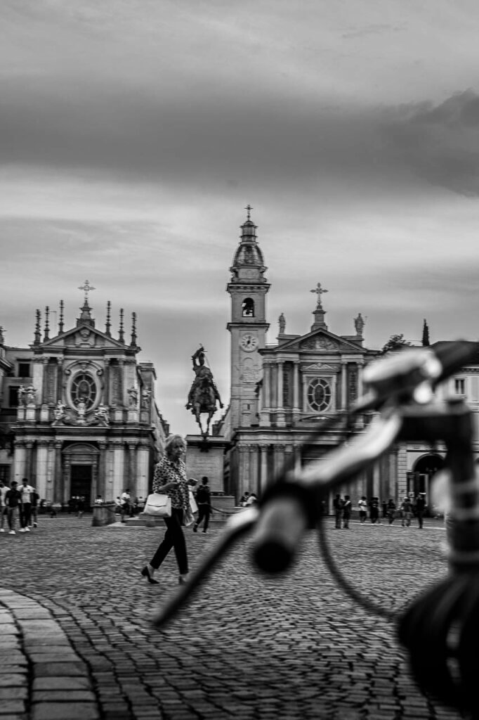 Photo in black and white of San Carlo square in Turin shows people walking and the churches in the background.